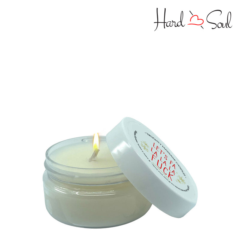 White Jar of Naughty Massage Candle Let's Fa La La La 1.7oz with the lid partially off, showing the candle lit inside - HardnSoul